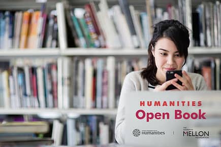 Female student looking at phone in a library with Humanities Open Book program logo overlaid on the image.