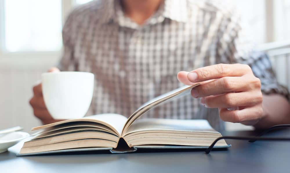 Close-up of a young man reading a book and drinking coffee.