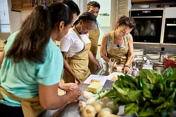 Side view of diverse group of men and women wearing aprons and standing at kitchen workstation as they participate in team building event.